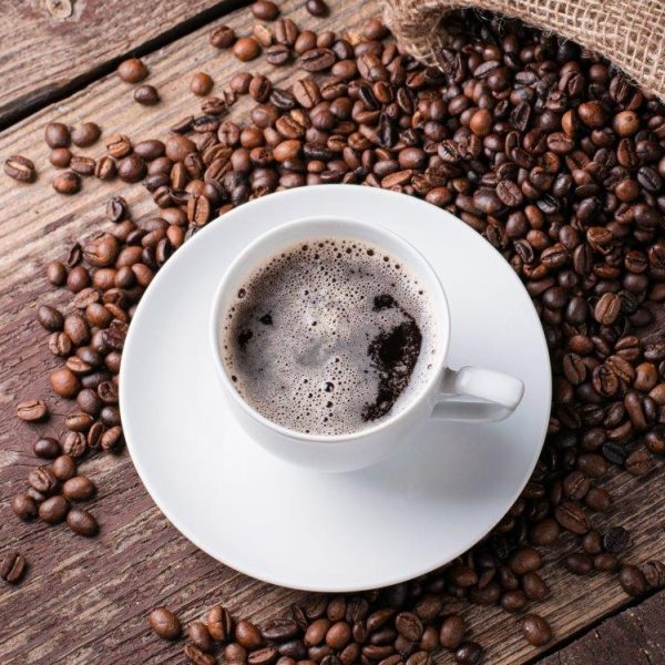 Tasse de café avec sous-tasse et grains de cafés étalés sur une table